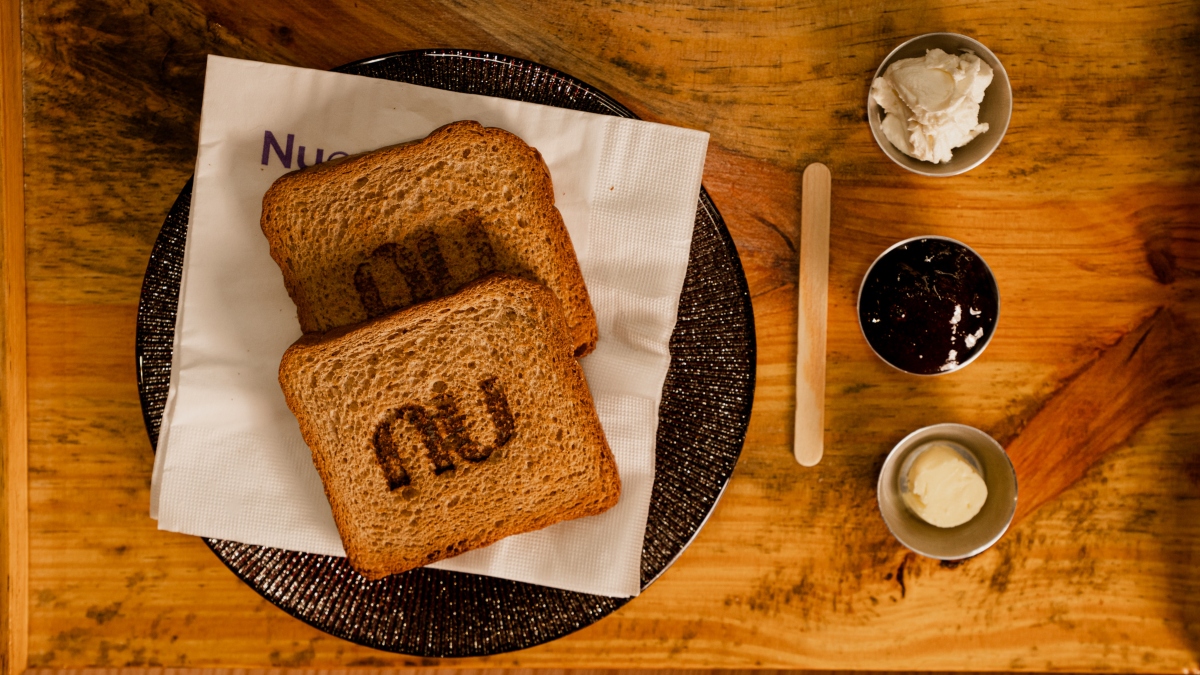 photo of a plate with toast in the center and three small pots (with butter, cream creese and jam). The toast has Nubank's logo highlighted